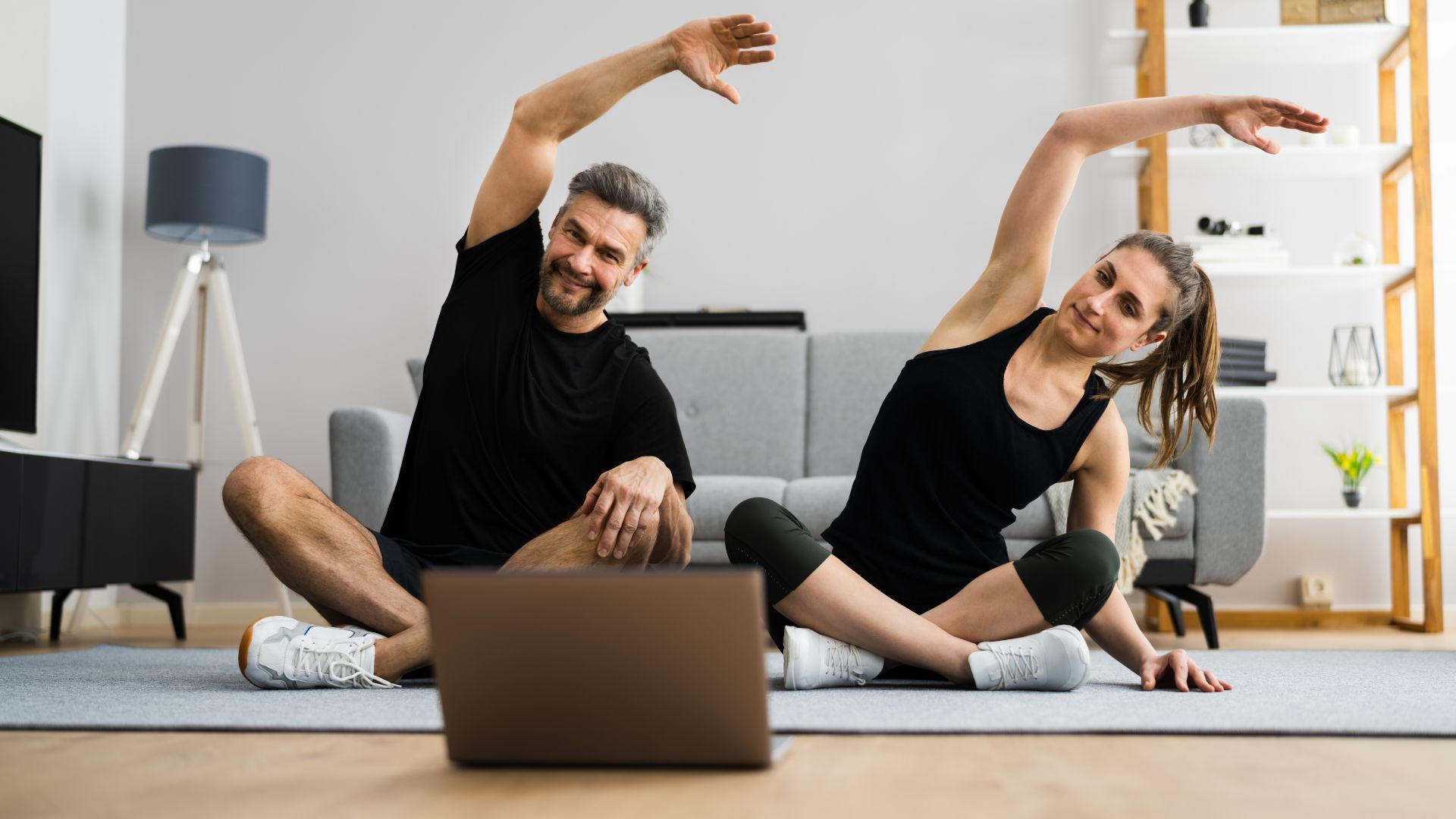 A middle aged couple working out at home to a video on a laptop.
