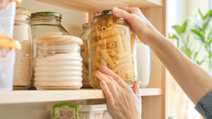 A woman replacing a container of dry pasta in her stocked pantry.